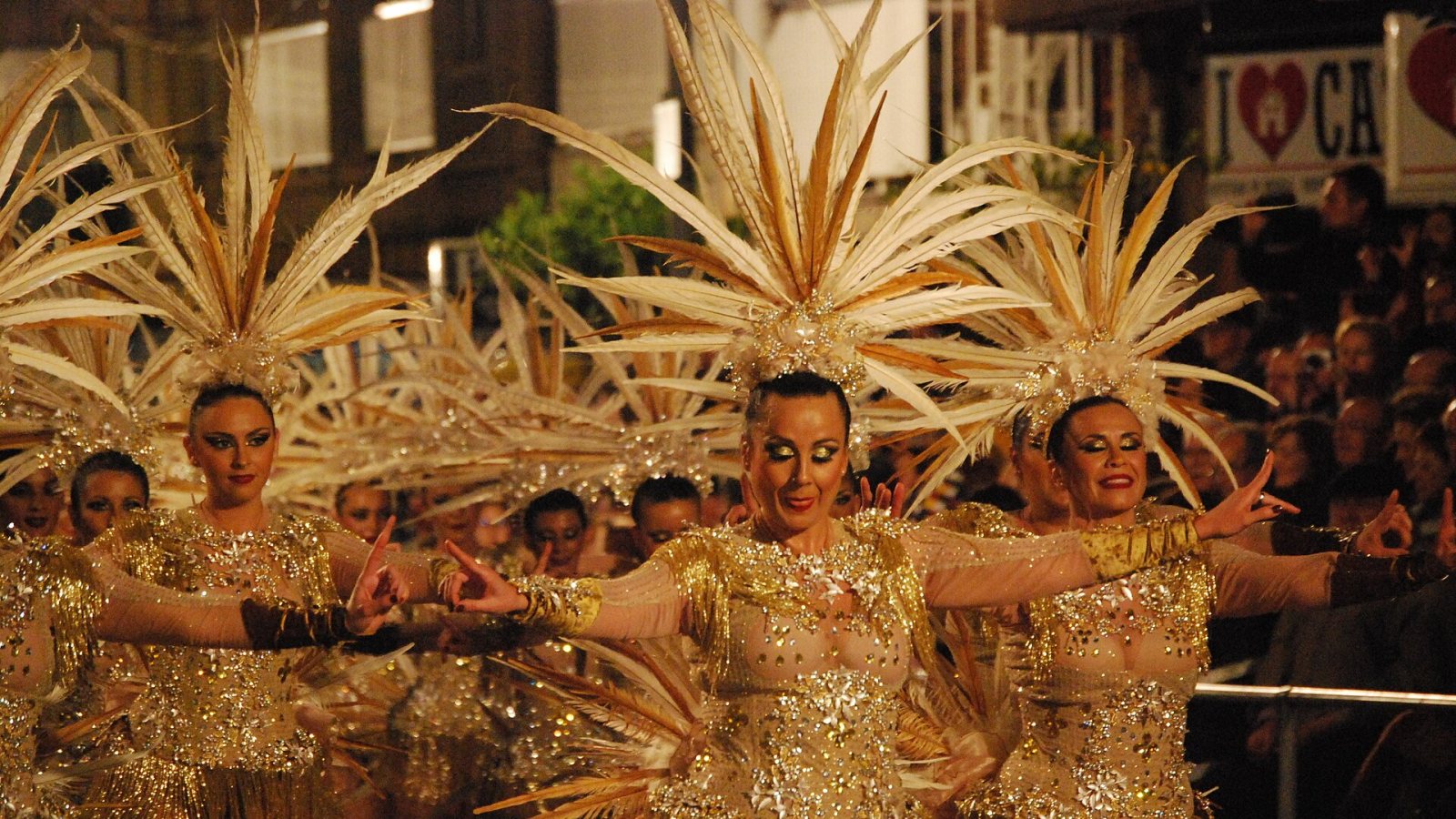Tänzerinnen in goldenen Kostümen mit großem Federschmuck beim Karnevalsumzug in Águilas.