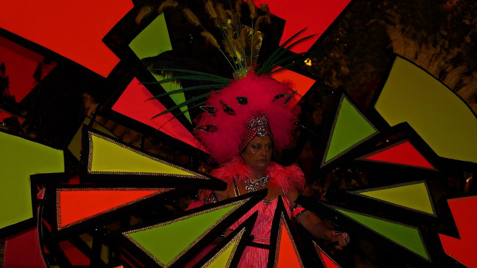 Karnevalskostüm mit rosa Federschmuck vor bunten geometrischen Flächen beim Karneval von Cartagena.