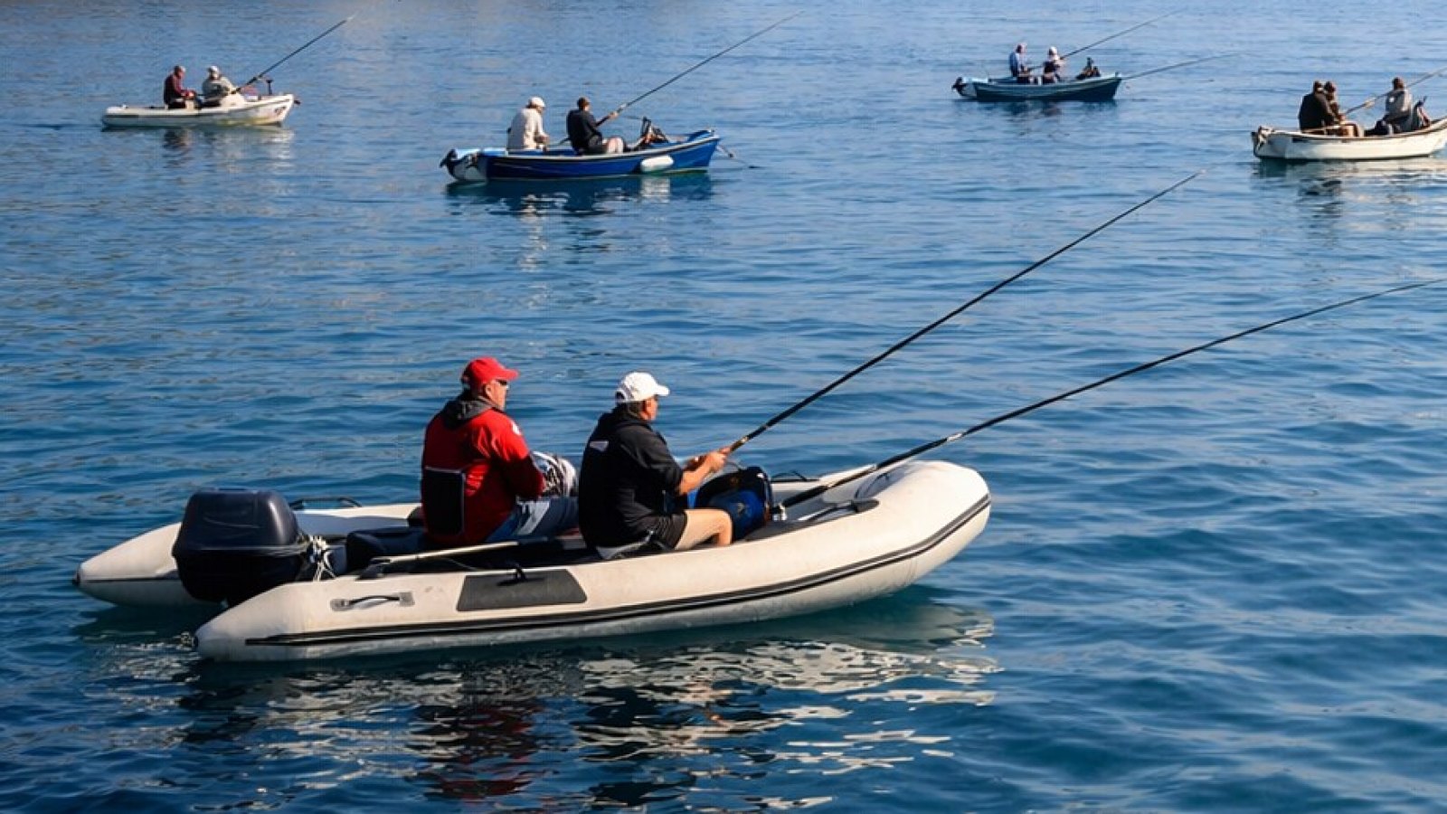 Angler mit langen Ruten in Schlauchboot und kleinen Booten auf ruhigem Meer (KI-Symbolbild).