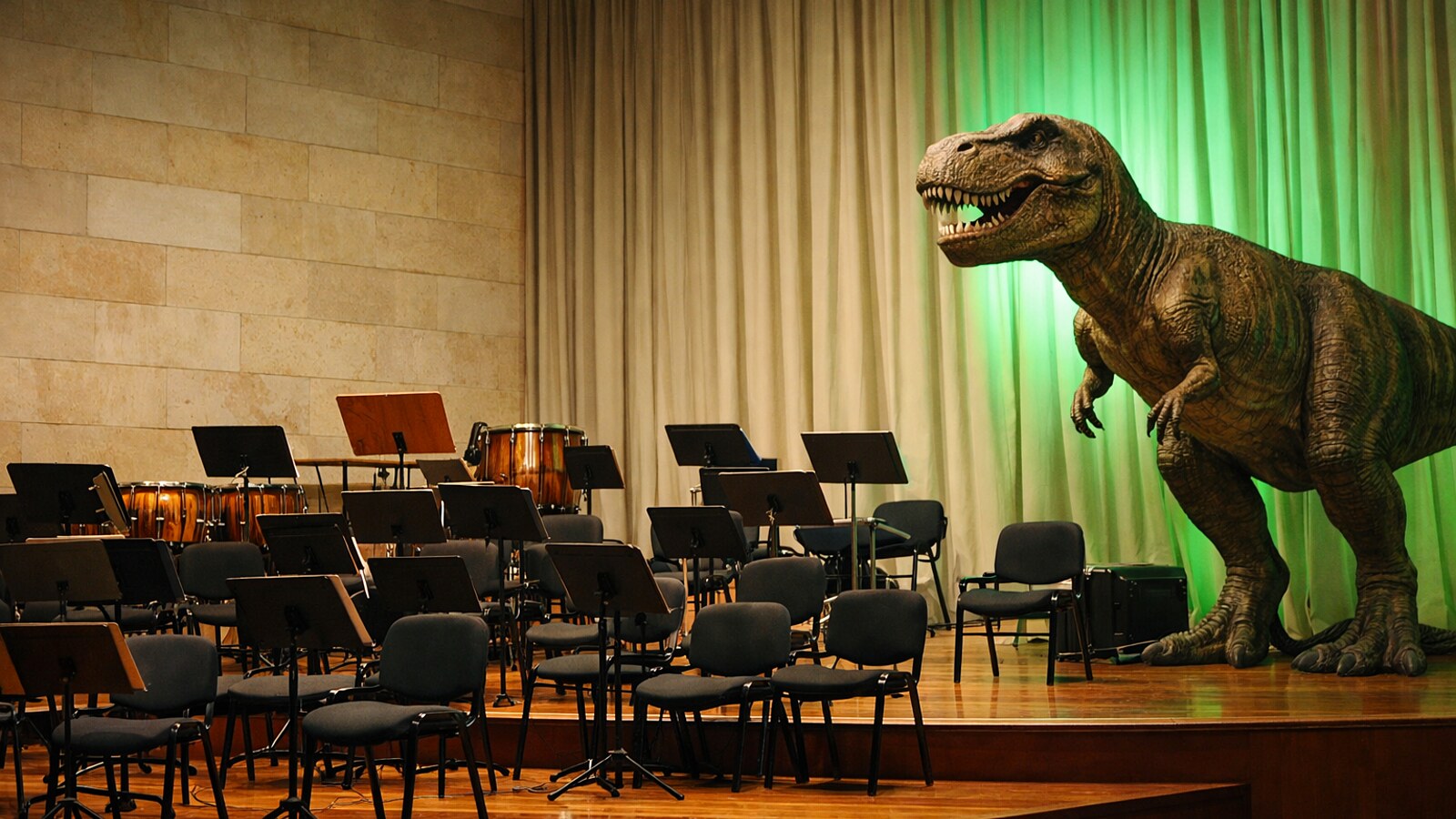 Großes Dinosauriermodell neben leeren Orchesterstühlen auf einer Konzertbühne (KI-Symbolbild).