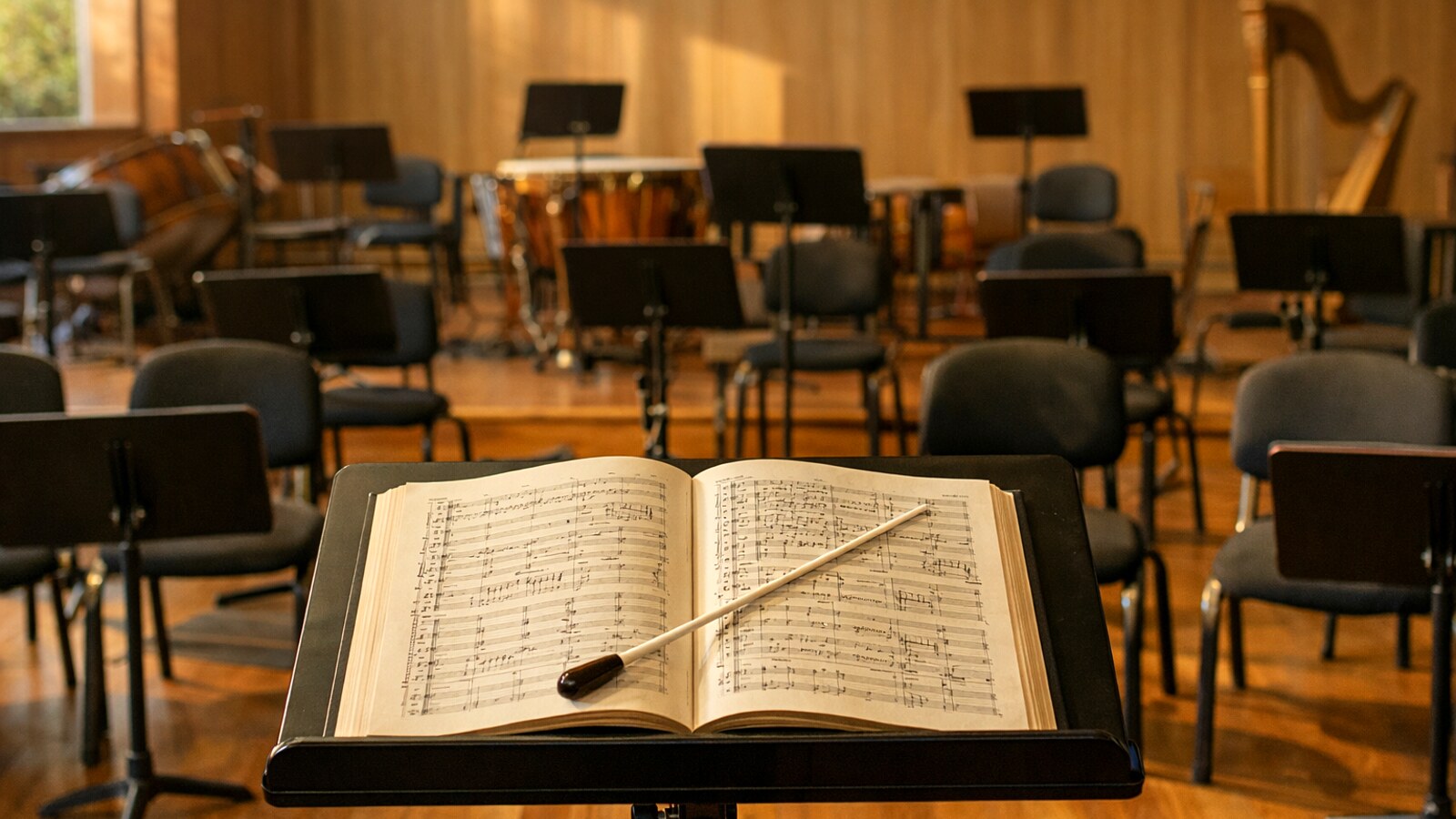 Dirigentenpult mit aufgeschlagener Partitur und Taktstock vor leeren Orchesterstühlen (KI-Symbolbild).
