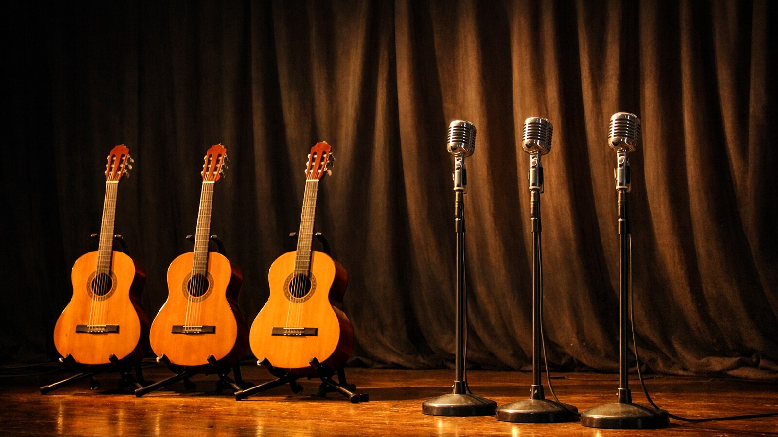 Drei Gitarren und drei alte Mikrofone nebeneinander auf einer Konzertbühne, ohne Menschen (KI-Symbolbild).