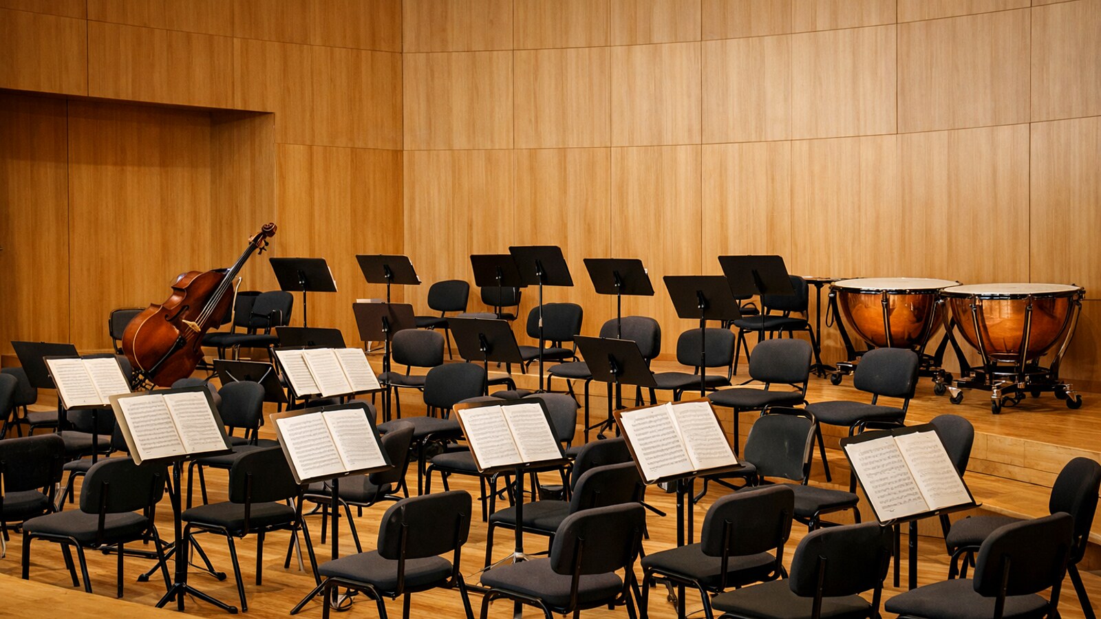 Leere Orchesterbühne im Konzertsaal mit Stühlen, Notenpulten, Kontrabass und Pauken (KI-Symbolbild).