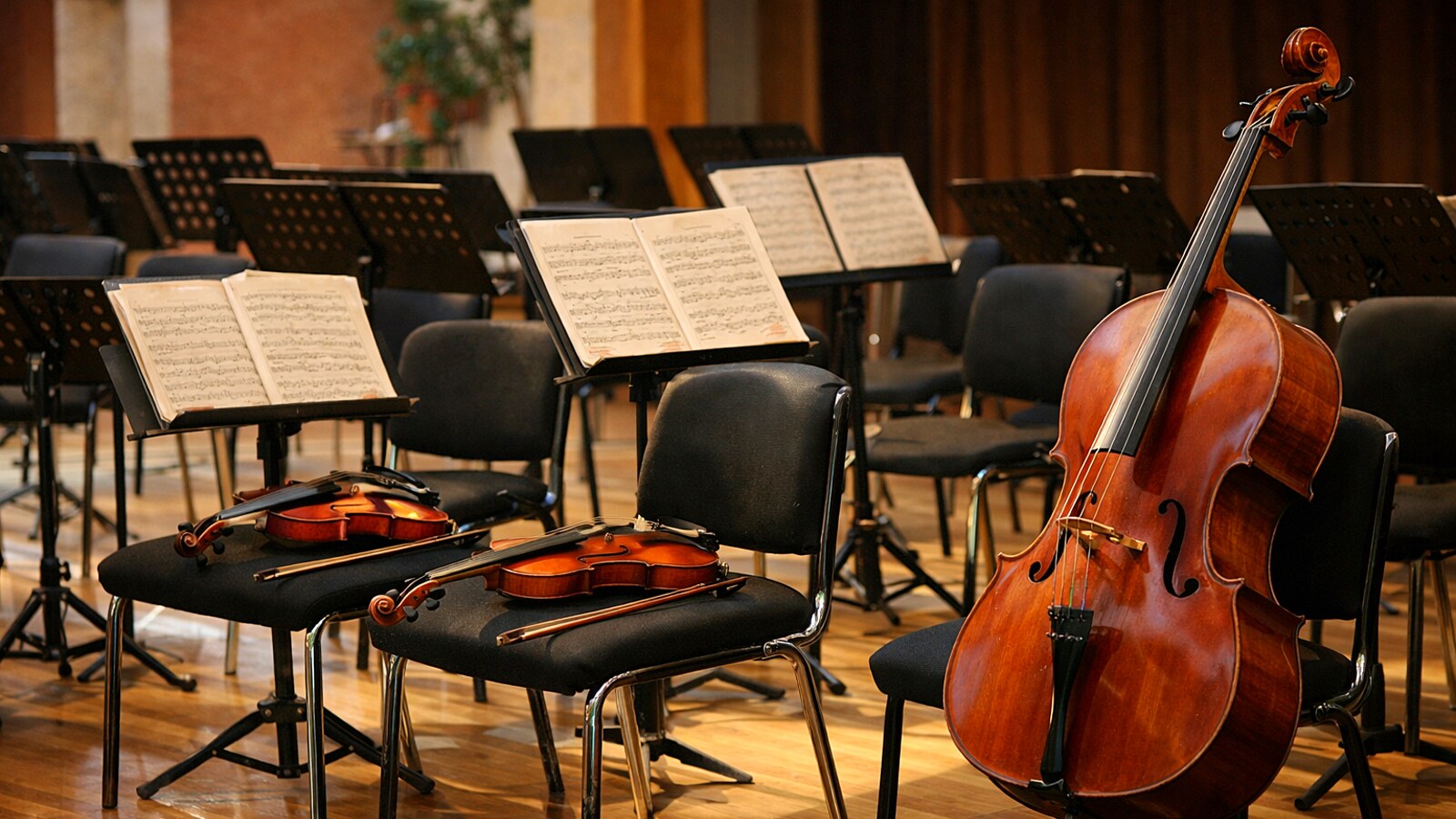Geigen und ein Cello auf den Stühlen eines Orchesters, Notenpulte mit Noten, ohne Menschen (KI-Symbolbild).