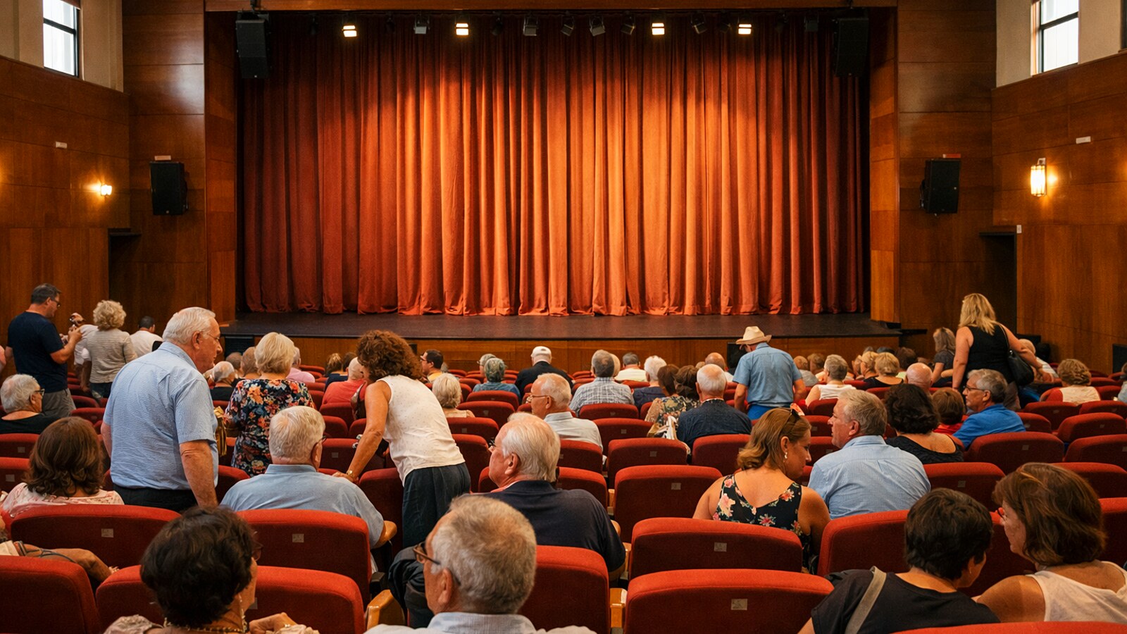 Publikum nimmt in einem Theatersaal vor geschlossenem Vorhang Platz (KI-Symbolbild).