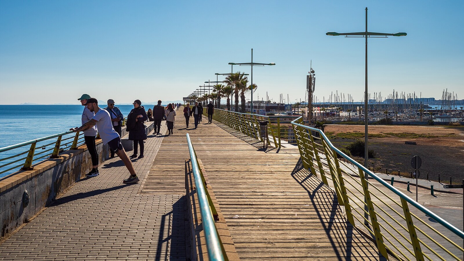 Spaziergänger auf dem Holzsteg der Hafenmole Dique de Levante in Torrevieja.