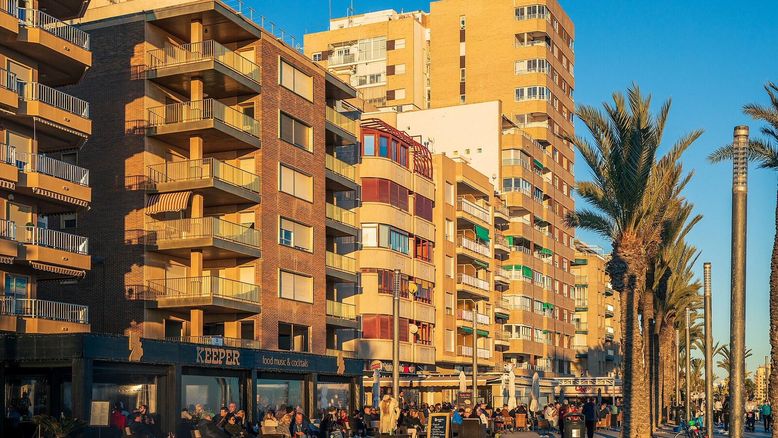 Belebte Terrassen und Palmen an der Promenade Paseo Juan Aparicio in Torrevieja im Abendlicht.