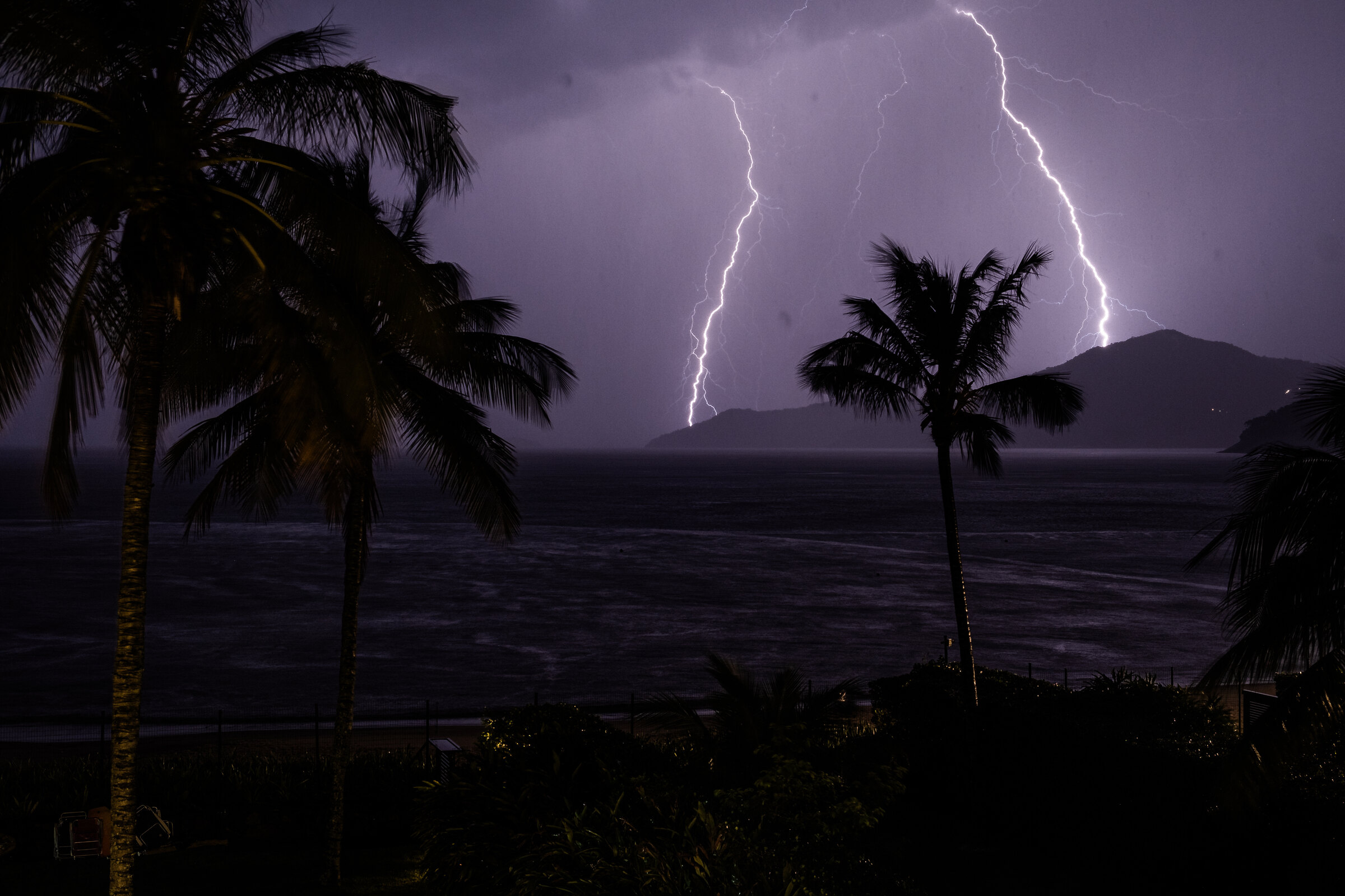 Blitze über dem Meer, Palmen im Vordergrund, Nacht. Wetter an der Costa Blanca und der Costa Cálida am 18.10.2026: Gewitter möglich, 21 bis 23 Grad.